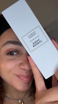 Białe, prostokątne pudełko na perfumy trzymane w górze, oznaczone napisem "Vanilla Nomad", o minimalistycznym designie i srebrnej obwódce; tło jest delikatnie rozmyte.