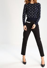 Mörkblå stickad tröja med vita mönster, parat med svarta slim fit-byxor och svarta spetsiga klackar, samt ett dekorativt vitt bälte.