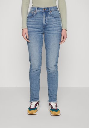 Jeans de tiro alto azul claro con un corte ajustado, que cuentan con un diseño clásico de cinco bolsillos y bajos deshilachados, combinados con zapatillas multicolores.
