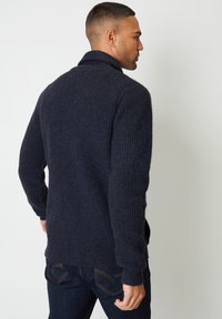 Cardigan in maglia a coste color blu navy con colletto alto, maniche lunghe e tasche laterali, realizzato in tessuto misto lana strutturato.