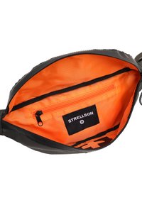 Schwarze Tasche mit einem orangen Stoffinnenraum, ausgestattet mit einer Reißverschlusstasche und einem Markenetikett. Glatte Außenseite mit einer dezenten Textur.