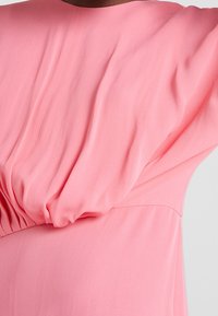 Růžová blůza s uvolněným střihem, měkkou tkaninou a nařasením v pase. Design má volné rukávy a hladkou texturu.