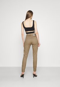 Svart ärmlös topp med en låg rygg, i kombination med ljusbruna tapered byxor, som har en patchlogga och dragkedjedetalj vid bakfickan.