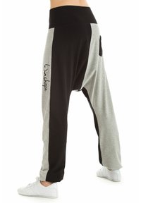 Črne in sivo harem-style hlače z širokim pasom, ki imajo stranske žepe in logotip na levi nogi. Mehka tekstura tkanine.