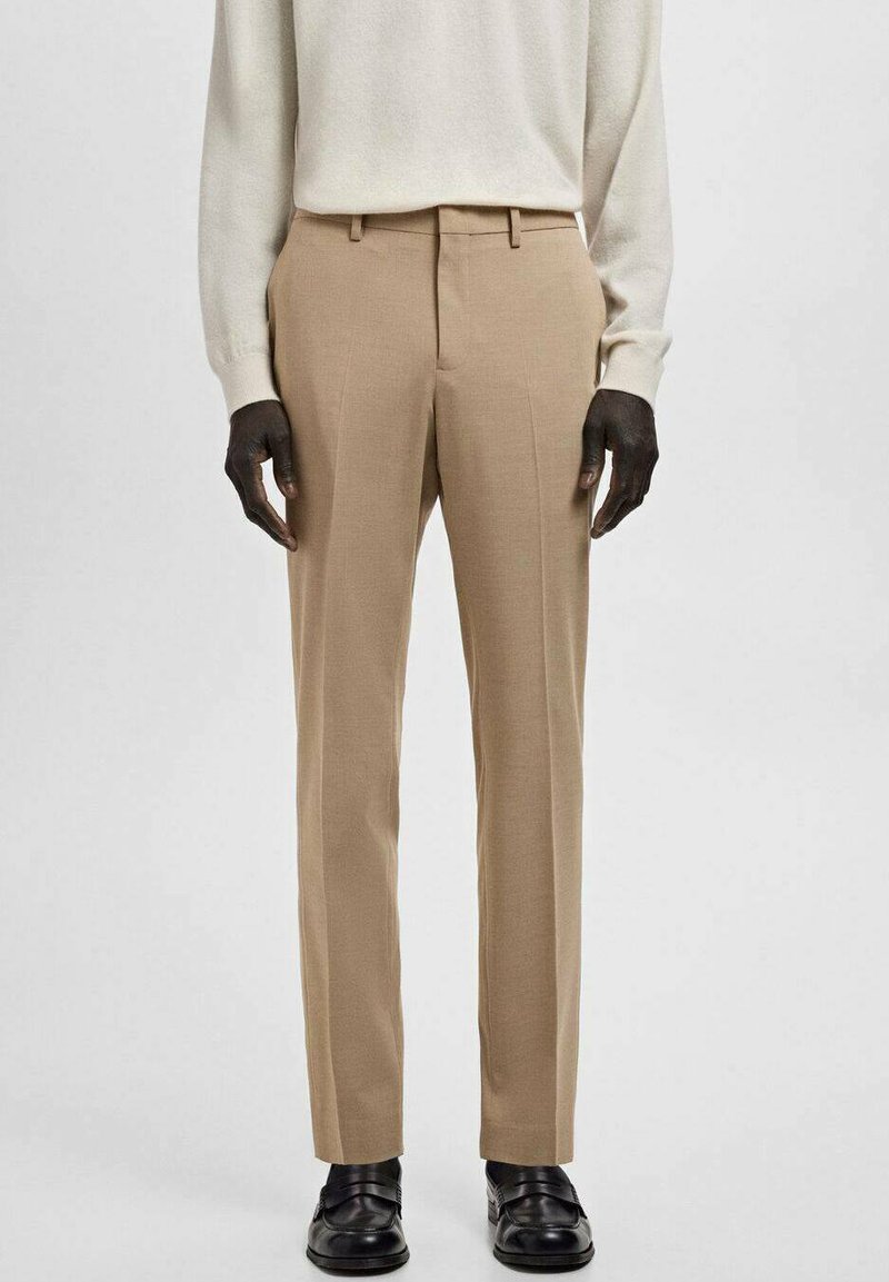 Pantalones beige a medida con corte recto, frente plano, trabillas para cinturón, bolsillos laterales y textura sutil, combinados con zapatos negros y un suéter ligero.