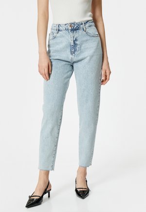 Jeans azzurri chiari a vita alta con taglio dritto, orlo sfilacciato e leggera scoloritura. Abbinati a décolleté neri a punta con cinturino alla caviglia.