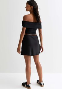 Zwarte off-shoulder top gecombineerd met een zwarte minirok. Glad, rekbaar materiaal met een aansluitend ontwerp. Eenvoudige silhouet, geaccentueerd met oorbellen.