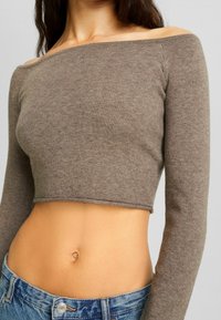 Top corto marrón con mangas largas acanaladas y escote a la altura de los hombros, combinado con jeans de mezclilla de cintura alta en azul claro.