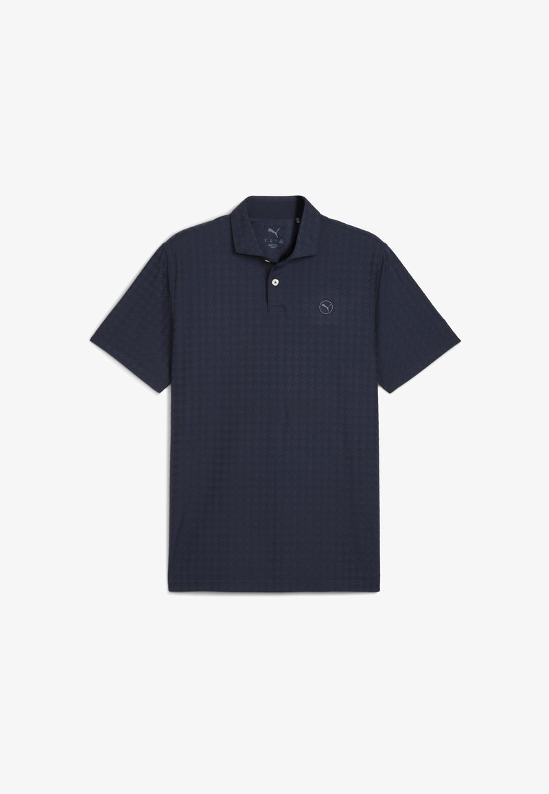 Tummansininen polo-paita, joka on valmistettu teksturoidusta kankaasta. Paitassa on kolme nappia ja pieni logo vasemmassa rinnassa. Lyhyet hihat.