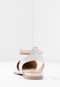 Białe skórzane sandały z otwartym tyłem, paskiem na kostkę, brązowym wnętrzem i okrągłym noskiem. Złoty klamra akcentująca na pasku.