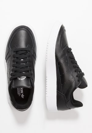 Sneakers in pelle nera con suola in gomma bianca, punta rotonda, sei occhielli e dettagli perforati sui lati. I lacci sono neri.