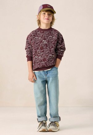 Bordeaux sweatshirt met witte handillustraties en de tekst "Pico bello"; lichtblauwe denim jeans; grijze sneakers met bruin accent; paarse pet.