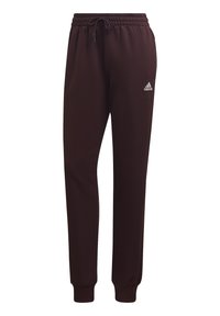 Pantalon de jogging Adidas marron foncé avec taille élastique, cordon de serrage, chevilles resserrées et logo Adidas blanc sur la cuisse gauche.