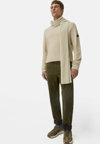Beige trui, geribbelde off-white sjaal, olijfgroene corduroy broek en bruine sneakers met donkere accenten. Eenvoudig, gelaagd outfit ontwerp.