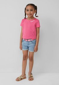 Roze katoenen T-shirt met drie witte hartontwerpen, gecombineerd met lichtblauwe denim shorts en gouden sandalen met kruisbanden.