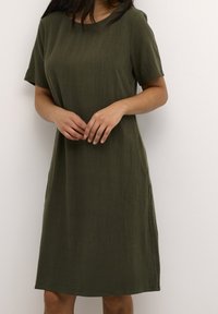 Vestido verde de manga corta hecho de una tela ligera y texturizada. Presenta un corte relajado y bolsillos laterales. Escote redondo, largo hasta la rodilla.