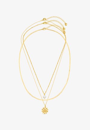 Collier superposé en ton or présentant deux styles de chaînes avec un accent en perle et un pendentif en forme de fleur à la base.