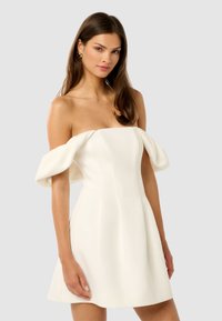 Vestido blanco off-the-shoulder con mangas abullonadas, corsé ajustado y falda acampanada; la textura suave y las líneas limpias crean una silueta moderna.