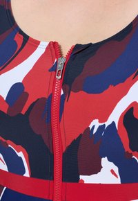Een kleurrijke zwemtop met een meerkleurig abstract patroon in rood, blauw en wit, met een centrale ritssluiting.