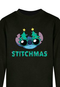 Čierna mikina s potlačou rozprávkového charakteru v slnečných okuliaroch, oblečeného v vianočných stromčekoch. Text pod obrazom znie "STITCHMAS" v farebných písmenách.