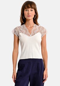 Top bianco con maniche corte in pizzo, scollatura a V, corpetto aderente e texture liscia, abbinato a pantaloni a palazzo blu navy.