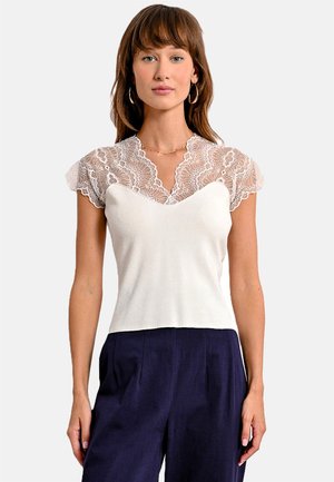 Top bianco con maniche corte in pizzo, scollatura a V, corpetto aderente e texture liscia, abbinato a pantaloni a palazzo blu navy.