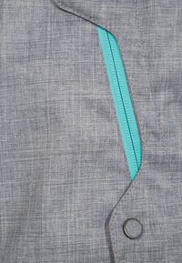 Szary materiał z turkusowym zamkiem częściowo otwartym na kieszeni kurtki, zabezpieczony czarnym zatrzaskiem.