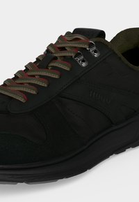 Baskets noires avec des lacets bordés de vert et de rouge, des œillets en métal et un marquage "HUGO" sur le côté et la languette.