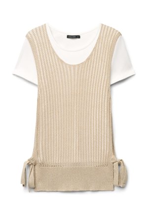 Beige gestrickte ärmellose Weste mit seitlichen Bändern, über einem weißen T-Shirt mit kurzen Ärmeln und rundem Ausschnitt getragen.