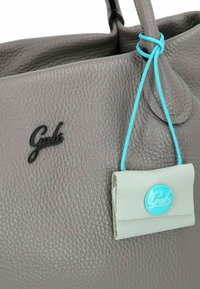 Grau strukturiert Weihnachtsanzug mit schwarzem Logo und einem hellblauen Anhänger, der mit einem dünnen blauen Kordel befestigt ist. Bemerkenswert für seine weiche, genoppte Oberfläche.