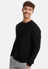 Zwarte lange mouwen shirt met een ronde hals, textuurmateriaal en minimale stikdetails, gecombineerd met lichtgrijze broek.