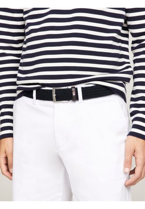 Person iført hvide bukser, navyblå og hvide striber langærmet skjorte samt et sort flettet bælte med sølvspænde.