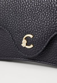 Portafoglio in pelle texturizzata blu navy con chiusura dorata caratterizzata da un design intrecciato a "C"; bordi lisci e dettagli di cucitura discreti.