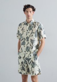 Short-sleeve shirt and shorts set in cream with dark green botanical print. Lightweight fabric, relaxed fit, button-down shirt design.