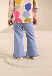 Svijetloplave plisirane trapezaste hlače s naboranim rubom, uparene s dugom majicom s rukavima ukrašenom šarenim velikim točkama.