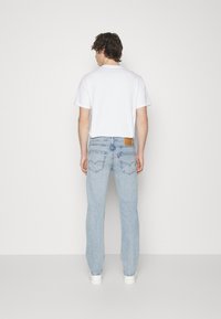 Lichtblauwe denimjeans met een rechte pijp, voorzien van achterzakken en een bruine leren label bij de taille. Gecombineerd met een wit T-shirt.