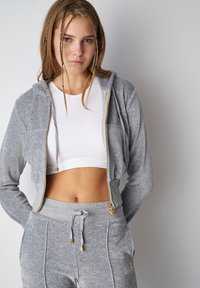 Gray zip-up hoodie with gold hardware, paired with a white ribbed crop top and gray sweatpants featuring drawstring and side pockets.