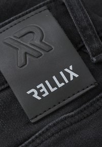 Schwarzer Denimstoff mit einem strukturierten schwarzen Lederpatch, das ein geprägtes Logo und den weißen Text "RELLIX" aufgestickt hat.