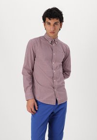 Camisa de cuadros rojos y azules con botones, de manga larga, cuello y corte ajustado. Combinada con pantalones azules de una tela suave.