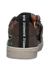 Grijze suède sneaker met zwarte mesh accenten, witte zool en een zwarte band met het etiket "BUNNIES.JR." Twee groene stippen zichtbaar nabij de hiel.