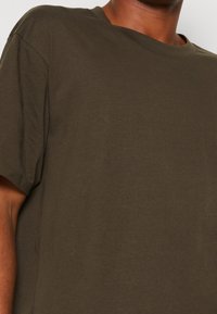 Close-up of a person wearing a plain olive green short-sleeve t-shirt with a round neckline.