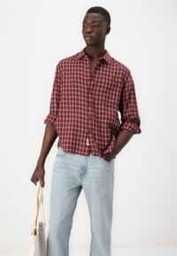 Rot-weiß karierter Hemd, Knopfverschluss-Stil, mit hochgekrempelten Ärmeln und einer Brusttasche, kombiniert mit hellblauen Jeans und einer Tragetasche.
