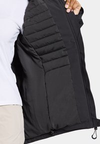 L'intérieur de la veste noire présente un rembourrage matelassé pour l'isolation, une texture de tissu lisse, une fermeture par bouton et un ourlet ajustable avec un cordon.