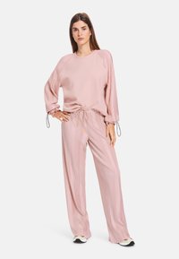 Helles rosa Loungewear-Set mit einem locker sitzenden Oberteil mit Raglanärmeln und Hose mit Kordelzug und vertikal geripptem Textur.