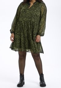 Groene luipaardprint jurk met lange mouwen, gelaagde rok en een gekartelde halslijn. Draagt het met zwarte enkelboots. Transparante, lichte stof.