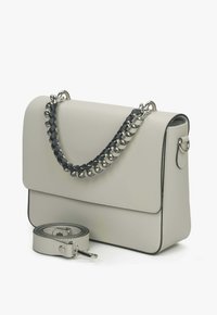 Šedá kožená kabelka s hladkým povrchem, černým a stříbrným řetízkem na držení a odnímatelným popruhem. Obsahuje klopový uzávěr a strukturovaný design.