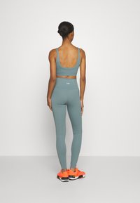 Turkusowy sportowy krótki top i legginsy z wysokim stanem, połączone z jaskrawo pomarańczowymi sportowymi butami. Gładka tkanina z dopasowanym krojem.