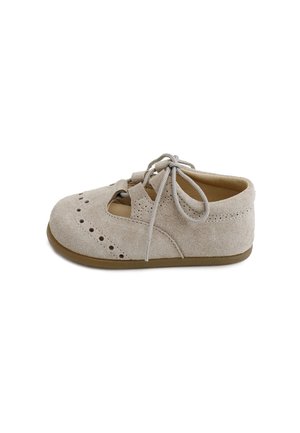 Zapato de bebé beige de ante con detalles perforados, tiras cruzadas y cordones atados sobre una suela marrón claro, mostrado de lado.