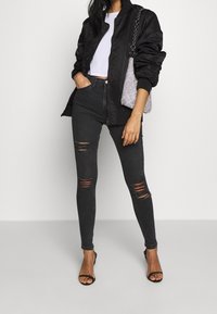 Svart bomberjacka, vit cropped topp, högmidjade svarta slitna jeans och svarta klackar med remmar. Väska med silverkedjedetaljer. Släta material.