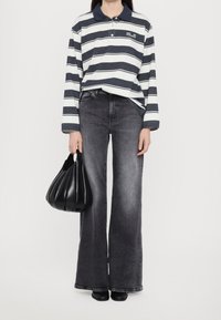 Polo shirt a righe blu navy e bianche con maniche lunghe, jeans grigi a vita alta e una borsa nera plissettata. Scarpe con tacco nere visibili.